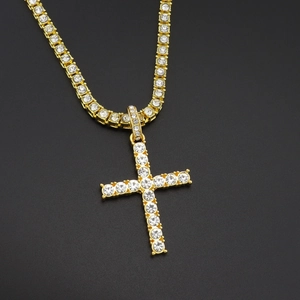 Gold tennis chain necklace with a large sparkling iced out cross pendant on black backdrop