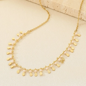 Close-up of gold chain necklace featuring delicate pink beaded fringe on a beige background