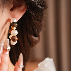 Detalle de pendientes de aro en C con perlas y piedras ojo de tigre alternadas