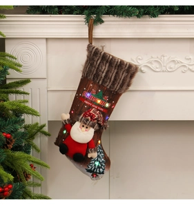 Lighted Christmas stocking with Santa Claus doll hanging by fireplace for holiday decor