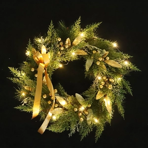 Christmas wreath with warm LED lights, gold berries, and ribbons on black background