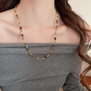 Gros plan du collier en perles d'oeil de tigre sur la clavicule avec détails dorés