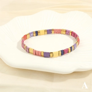 Macro view of multi-color enamel Tila bead bracelet with gold accents on silk