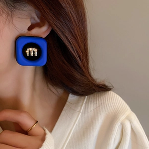 Close-up of model wearing blue square chain earrings with a sparkling rhinestone letter M