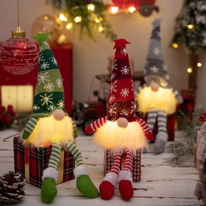 Close-up of three glowing Christmas gnomes with knitted snowflake hats and LED lights
