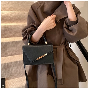 Detail of lychee textured black crossbody bag with golden hardware and top handle strap