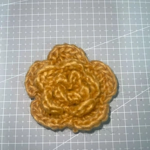 Detailed view of a 7cm golden three-layer crochet flower on a grey cutting mat