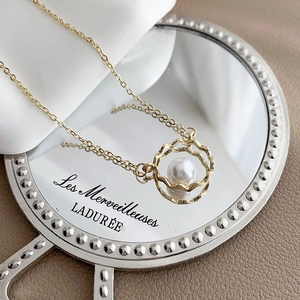 Detail of a gold double-wave pendant necklace with a pearl on a vintage handheld mirror