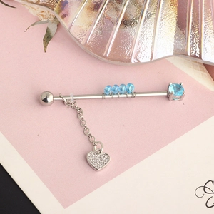 Detailed macro shot of a silver industrial barbell featuring blue gems and a heart charm
