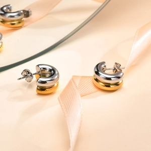 Detailed macro view of two-tone gold and silver C-shaped chunky earrings on pink ribbon