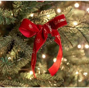 Red velvet Christmas bow with gold Merry Christmas print hanging on a decorated tree branch