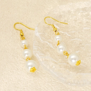 Elegant long drop earrings with three white pearls and gold accents on textured fabric