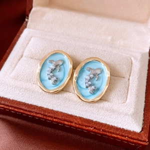 Macro detail of oval gold earrings with blue enamel, silver dolphin and pearl accents