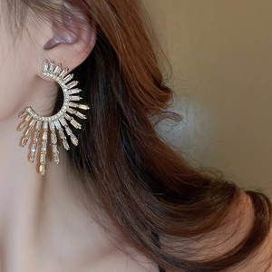 Close-up of golden C-shaped earrings with radiating rectangular zircons on a model