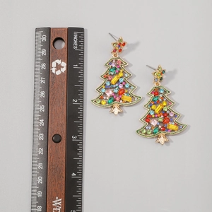 Detail view of Christmas tree earrings with colorful rhinestones next to a measuring ruler
