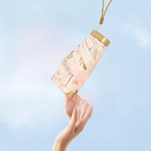 Lightweight 230g floral sun umbrella with gold lanyard held against a clear blue sky