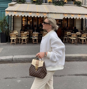 Street style view of a white sherpa bomber jacket paired with a checkerboard handbag