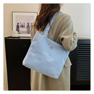 Detail of light blue corduroy tote bag with Fashion Institute label shown on model