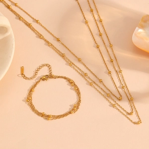 Three-layer gold titanium steel beaded necklace and bracelet set on an elegant background