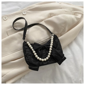 Detail of black satin shoulder bag with a large bow and elegant pearl chain strap