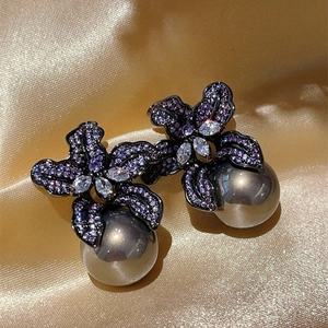 Close-up of luxury purple lily earrings with pavé crystals and dark grey pearls on satin