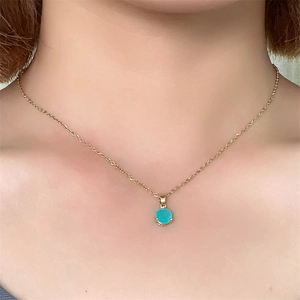 Close-up of a minimalist gold necklace with a round turquoise zircon pendant on neck