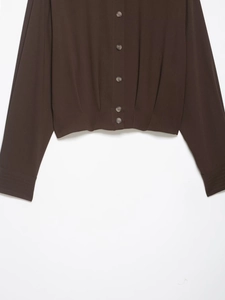 Detail of dark brown shirt featuring buttoned cuffs and waist pleats on woven fabric