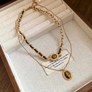 Détail de colliers dorés vintage avec pierre œil de tigre et chaîne tressée en cuir