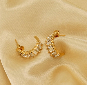 Detail view of gold-plated C-shaped earrings with square zircon on champagne satin