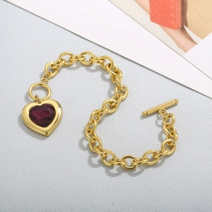 Detail of gold chain bracelet with heart-shaped purple crystal and toggle OT clasp