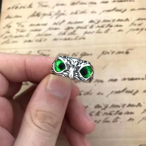 Vintage silver owl ring with green gemstone eyes shown against a retro script background