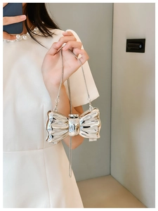 Glossy silver bow-shaped mini bag with metallic chain strap worn by a model