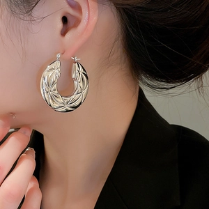 Detail of silver hoop earring with radial engraved texture worn by a model in black