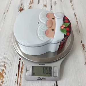 Detailed view of Santa Claus tin box on kitchen scale showing actual weight of 85.8g