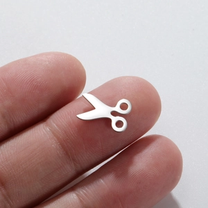 Macro shot of a tiny polished stainless steel scissor charm held on a fingertip