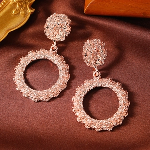Macro shot of rose gold earrings with crumpled metal texture on silk background