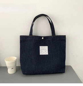 Detail of dark blue denim tote bag with cute bear patch and secure metal snap closure