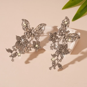 Silberne Ohrclips mit Schmetterling und Blumenmotiven auf einem Steinpodest präsentiert