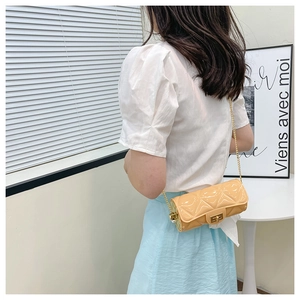 Quilted beige cylindrical chain bag worn by model in a minimalist indoor setting
