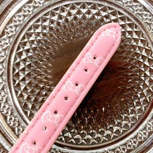 Close-up of pink watch strap with white bow pattern on a textured glass surface