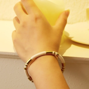 Detail of bamboo-style gold-plated titanium steel bracelet with white enamel splice