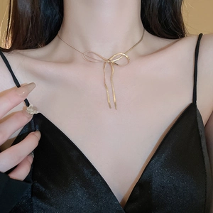 Detail of a gold snake chain necklace with a hollow bow pendant on a model's neck