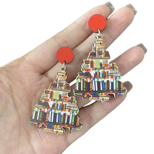 Detail of colorful stacked book Christmas tree earrings held in hand against white background
