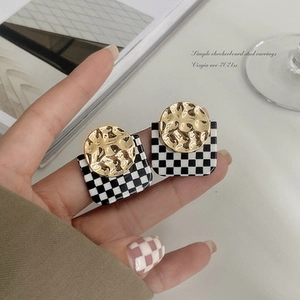 Close-up of checkerboard stud earrings with textured gold metal center details