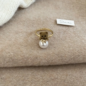 Detail of 18K gold plated ring with brown flocked bear and white pearl on beige fabric