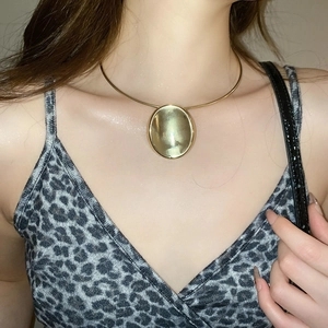 Detail of a minimalist golden large circular pendant necklace on model showing its metallic glow