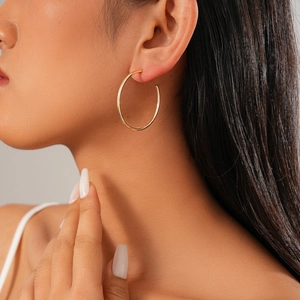 Close-up of minimalist golden circular geometric hoop earring worn by a model