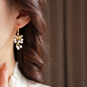 Detail van elegante vlinderparel oorbellen met 18K goudlaag gedragen door een model