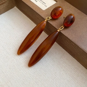 Detailed close-up of amber tortoiseshell acrylic water drop earrings with golden links