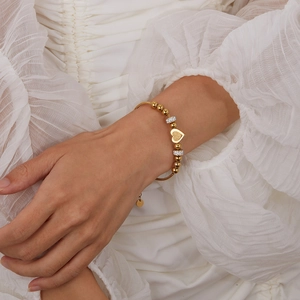 Close-up of golden beaded bracelet with frosted heart charm and zircon details worn on wrist